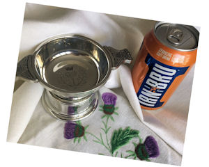Thistle engraved quaich and can of Irn-Bru on
                  a cream linen tablecloth embroidered with purple
                  thistles
