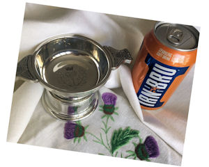 Thistle engraved quaich and can of Irn-Bru on
a cream linen tablecloth embroidered with purple
thistles